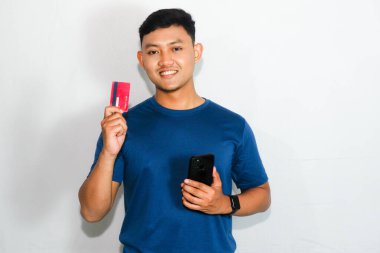 Cep telefonu tutarken kredi kartı gösteren mavi tişörtlü genç Asyalı adam.