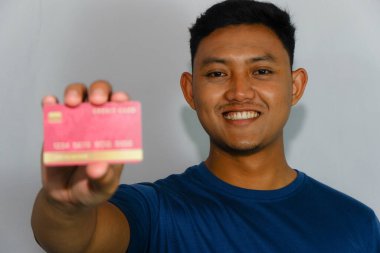 Mavi gömlekli genç Asyalı adam kredi kartını gösteriyor.