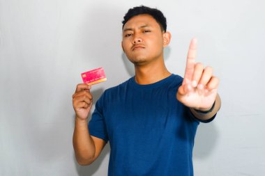 Mavi gömlekli genç Asyalı adam kredi kartı gösteriyor ve içki yasağı hareketi yapıyor.