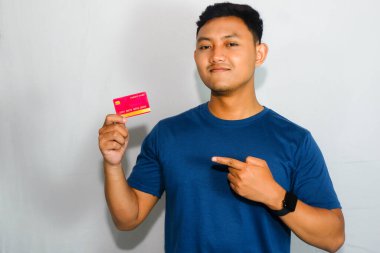 Mavi tişörtlü genç Asyalı adam sakin yüzlü kredi kartı gösteriyor.