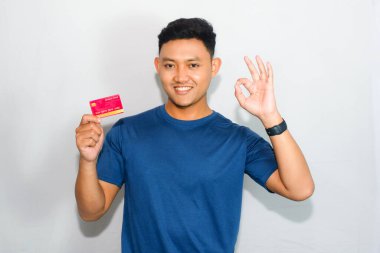 Mavi gömlekli genç Asyalı adam kredi kartı gösteriyor ve iyi bir jest yapıyor.