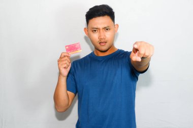 Mavi tişörtlü genç Asyalı adam kredi kartı gösteriyor ve kameraya işaret ediyor.