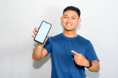 Mavi tişörtlü, boş akıllı telefon ekranı gösteren dost canlısı Endonezyalı genç adam.