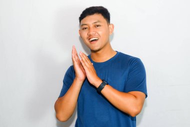 Asyalı adam mavi tişört giyip mutlu yüzlü el çırpıyor.