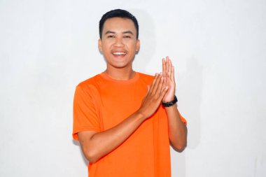 Turuncu tişört giyen Asyalı adam alkışlıyor ve gülümsüyor.