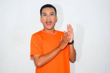 Turuncu tişört giyen Asyalı adam alkışlıyor ve gülümsüyor.