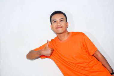 Turuncu tişört giyen Asyalı adam yan taraftan baş parmak hareketi yapıyor.