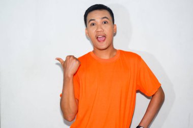 Dost canlısı, turuncu tişörtlü bir Asyalı başparmağı ve ağzı açık bir şekilde yan tarafı işaret ediyor.