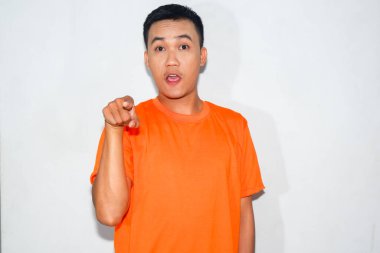 Dost canlısı, turuncu tişörtlü, kafası karışmış, ileriye bakan Asyalı bir adam.