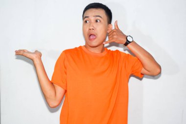 Dost canlısı, turuncu tişörtlü, kafası karışık Asyalı bir adam telefon konuşması yapıyor.