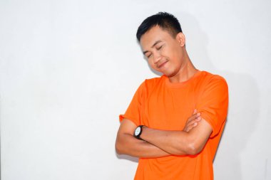 Dost canlısı Asyalı adam turuncu tişört giyiyor ve gülümsüyor.