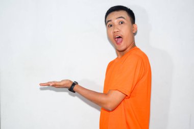 Turuncu tişört giyen hevesli Asyalı bir adam, dostane bir ifadeyle ürünü gösteren bir jest yapıyor..