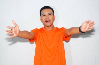 Turuncu tişört giyen heyecanlı bir Asyalı adam, mutlu bir ifadeyle sarılmak ya da selamlaşmak istediğini gösterir.