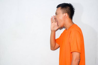 Heyecanlı Asyalı adam turuncu tişört giyiyor. Şok olmuş yüz ifadesi var. Çığlık atıyor.