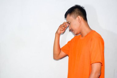 Heyecanlı Asyalı adam turuncu tişört giyiyor ve hayal kırıklığına uğramış bir ifade takınıyor. Düşünme hareketi yapıyor.