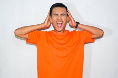 Heyecanlı Asyalı, turuncu tişörtlü, sinirli bir ifade takınarak kulak hareketi yapıyor.