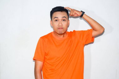 Heyecanlı Asyalı adam turuncu tişört giyiyor ve kafası karışık jestler yapıyor.