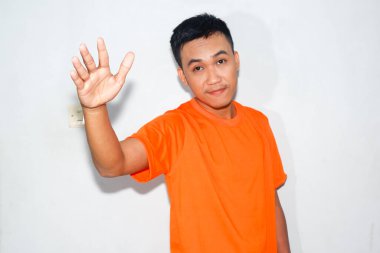 Turuncu tişört giyen heyecanlı bir Asyalı dost canlısı ve korkmuş bir ifadeyle selam veriyor ya da selam veriyor.