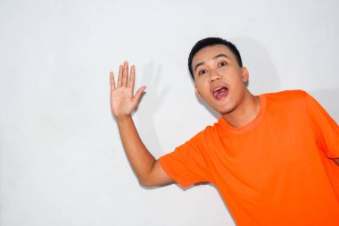 Heyecanlı, turuncu tişört giyen Asyalı bir adam yandan karşılama jesti yapıyor.