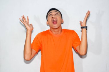 Heyecanlı Asyalı adam turuncu tişört giyiyor ve yukarıdan bir hediye düşmesi jesti yapıyor.