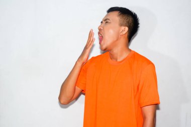 Heyecanlı Asyalı bir adam turuncu tişört giyiyor ve uykulu bir ifade sergiliyor.