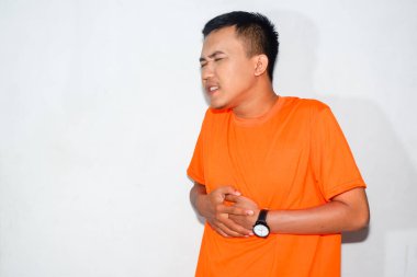 Heyecanlı Asyalı adam turuncu tişört giyiyor ve rahatsız edici bir ifade takınıyor.