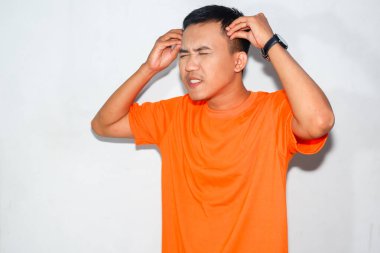 Heyecanlı Asyalı adam turuncu tişört giyiyor ve sinirli bir ifade takınıyor.