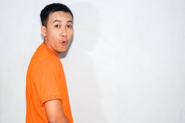 Heyecanlı Asyalı adam turuncu tişört giyiyor ve komik bir ifade takınıyor.