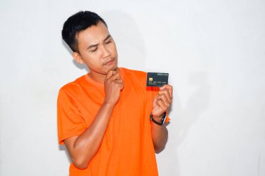 Turuncu tişört giyen kafası karışmış Asyalı bir adam kredi kartına bakıyor..