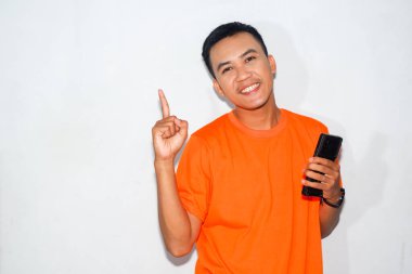 Dost canlısı, turuncu tişörtlü, akıllı bir telefon tutan ve yukarıyı gösteren Asyalı bir adam. Başarı kavramı, başarı, olumlu mesaj veya bilgi paylaşımı