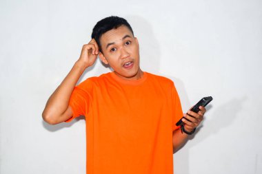 Dost canlısı, turuncu tişörtlü, akıllı telefon tutan ve kafasına dokunan Asyalı bir adam. Akıllı telefon kullanırken düşünme, kafa karıştırma ya da düşünme kavramı