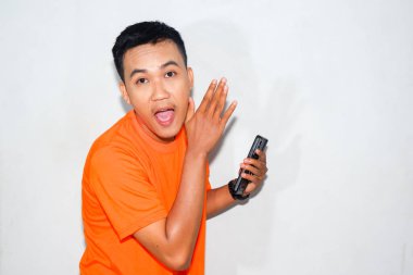Dost canlısı, turuncu tişörtlü, elinde akıllı bir telefon olan Asyalı bir adam bir jest yapıyor. Bilgi paylaşım, iletişim veya dijital etkileşim kavramı