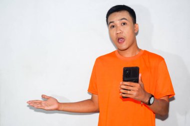 Dost canlısı, turuncu tişörtlü, akıllı telefon tutan ve parmağıyla kenarı gösteren Asyalı bir adam. Yön kavramı, dijital etkileşim veya rehberlik