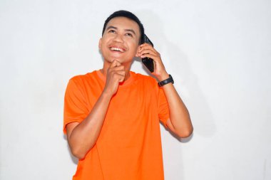 Dost canlısı, turuncu tişörtlü, telefonda konuşan ve düşünen Asyalı bir adam. İletişim, tefekkür veya karar verme kavramı