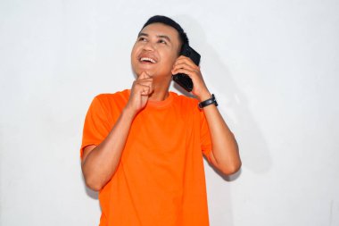 Dost canlısı, turuncu tişörtlü, telefonda konuşan ve düşünen Asyalı bir adam. İletişim, tefekkür veya karar verme kavramı