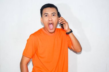 Turuncu tişört giyen, telefonda konuşan ve bağıran Asyalı bir adam. Bir telefon konuşması sırasında şok, heyecan ya da duygusal tepki kavramı