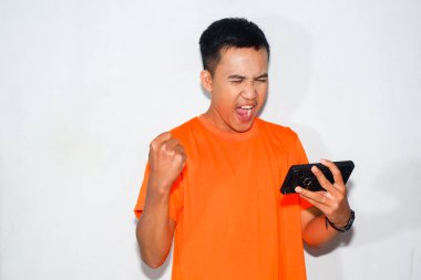 pria asia dengan ekspresi berteriak bahagia memakai kaos orange sedang melihat pertangan streaming di smartphonenya
