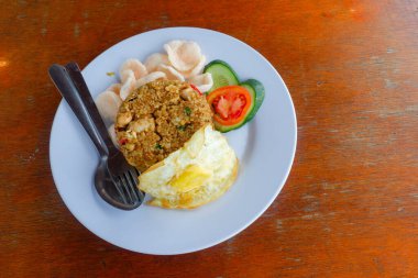 Bir tabak kızarmış Endonezya pilavı (nasi goreng) kızarmış yumurta, karides krakeri, salatalık ve domates dilimleri ile servis edilir.