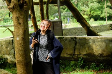 Göl kenarında seyahat ederken elinde akıllı telefon tutan bir kadın. Dijital yaşam tarzı, doğa turizmi ve açık hava rahatlama kavramı