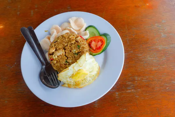 Bir tabak kızarmış Endonezya pilavı (nasi goreng) kızarmış yumurta, karides krakeri, salatalık ve domates dilimleri ile servis edilir.