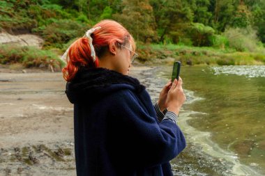 Kadın akıllı telefonunu kullanarak gölün fotoğrafını çekiyor. Doğa fotoğrafçılığı, seyahat ve dijital yaşam tarzı kavramı