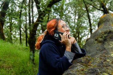 Ormanda tatildeyken Asyalı bir kadın telefonda konuşuyor. İletişim, seyahat ve doğa yaşam tarzı kavramı