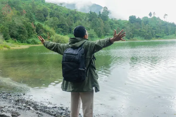Sırt çantalı adam, kollarını açmış tatildeyken gölün tadını çıkarıyordu. Özgürlük, macera ve doğa yolculuğu kavramı