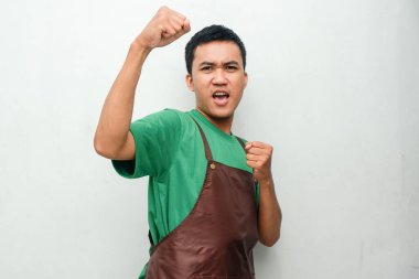 Yeşil gömlekli ve kahverengi önlüklü genç adam coşkulu bir ifadeyle zafer kutlaması yapıyor. Başarı, neşe ve pozitif enerji kavramı