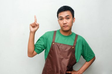 Yeşil tişörtlü ve kahverengi önlüklü gülümseyen Asyalı genç bir adam dostça bir ifadeyle yukarıya doğru bakıyor. Hizmet, promosyon veya pozitif mesaj temaları için ideal