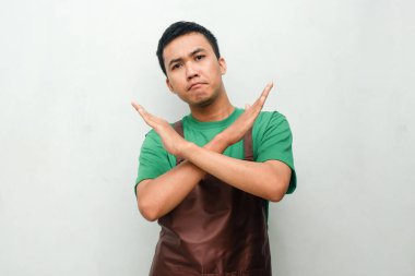 Yeşil gömlekli ve kahverengi önlüklü genç adam rahatsız edici bir ifade takınıyor ya da jesti durduruyor.