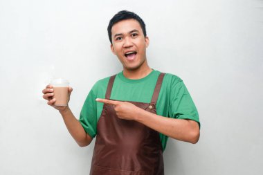 Yeşil tişörtlü ve kahverengi önlüklü gülümseyen Asyalı genç adam dostça ve coşkulu bir ifadeyle başparmak kaldırıyor. Servis, kafe veya tanıtım temaları için mükemmel