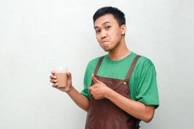 Yeşil tişörtlü ve kahverengi önlüklü gülümseyen Asyalı genç adam dostça ve coşkulu bir ifadeyle başparmak kaldırıyor. Servis, kafe veya tanıtım temaları için mükemmel