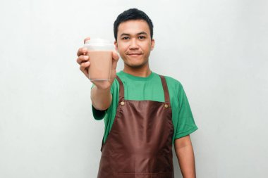 Yeşil tişörtlü ve kahverengi önlüklü gülümseyen Asyalı genç adam dostça ve coşkulu bir ifadeyle başparmak kaldırıyor. Servis, kafe veya tanıtım temaları için mükemmel