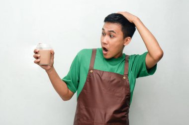 Yeşil tişörtlü ve kahverengi önlüklü gülümseyen Asyalı genç adam dostça ve coşkulu bir ifadeyle başparmak kaldırıyor. Servis, kafe veya tanıtım temaları için mükemmel